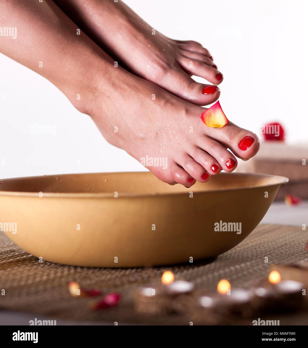 I piedi femminili con gocce di acqua spa ciotola, asciugamani, fiori, candele, sale marino e una bottiglia di olio essenziale su sfondo bianco. Piedi spa concept. Foto Stock