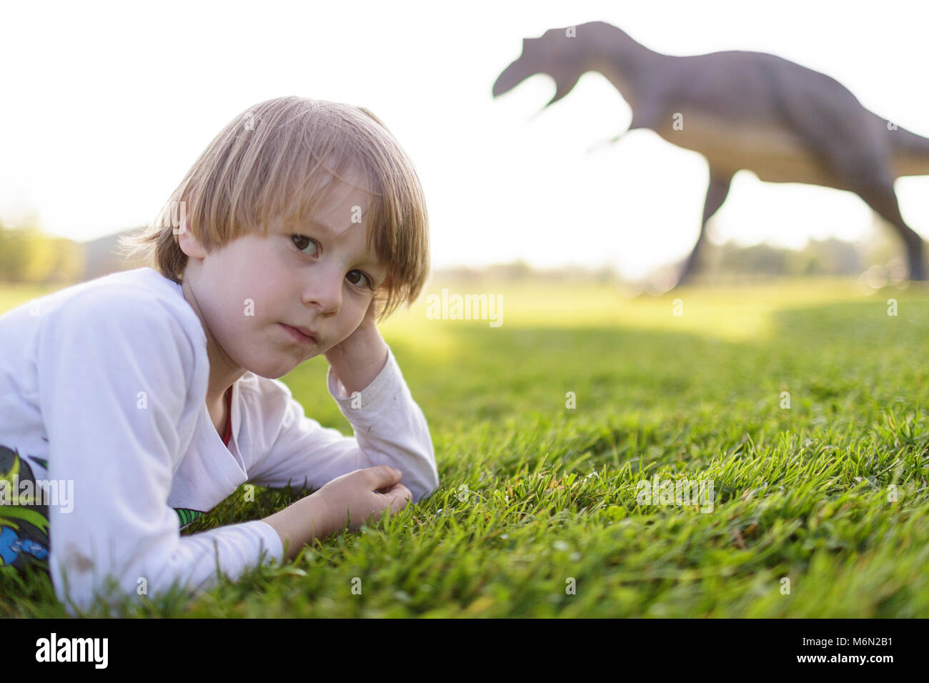 Little Boy sdraiati sull'erba nel parco con i dinosauri in esterno Foto Stock