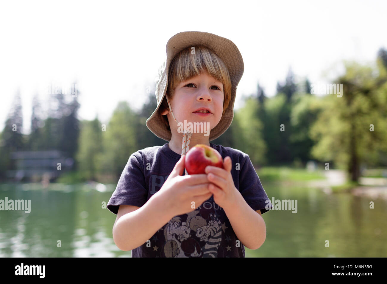 Agricoltura - un ragazzino con un cappello trattiene e mangia una mela fresco dal lago di Bled Slovenia, Europa Foto Stock