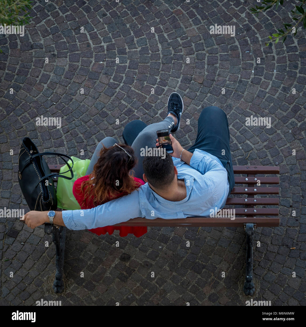 Giovane seduto su un banco di lavoro guardando il telefono cellulare dal di sopra Foto Stock