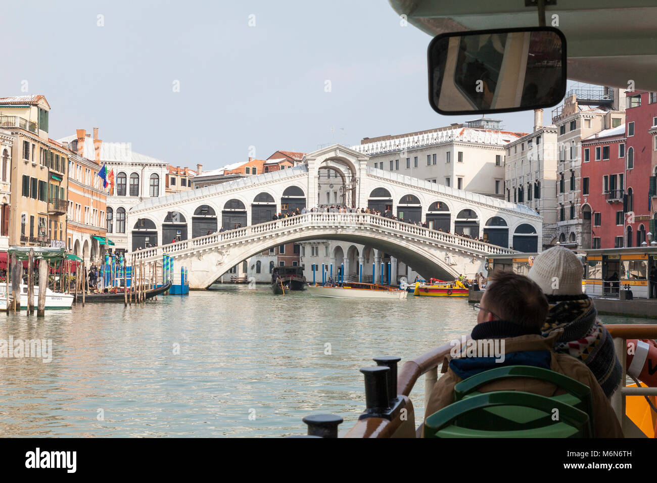 I turisti su un vaporetto percorre il Canal Grande e il Ponte di Rialto, Venezia, Italia in inverno con neve sui tetti, prima persona POV oltre la prua Foto Stock