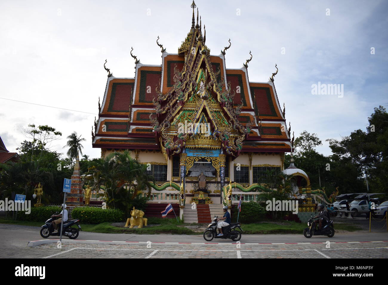Tre scooter a uguale distanza passando da una sontuosa thailandese tempio buddista centrato con un cielo blu sullo sfondo. Wat Laem Suwannaram, Bo Phut. Foto Stock