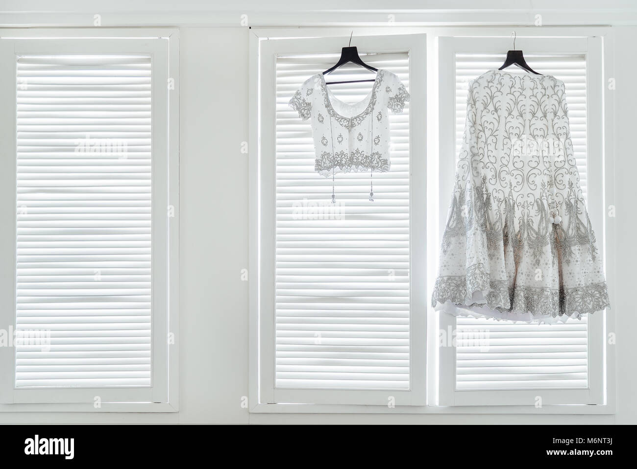 L'indiano abito da sposa, saree e camicetta appesa con le finestre bianche con luce in background. Foto Stock L'indiano abito da sposa, saree e camicetta appesa con le finestre bianche con luce in background. Foto Stock