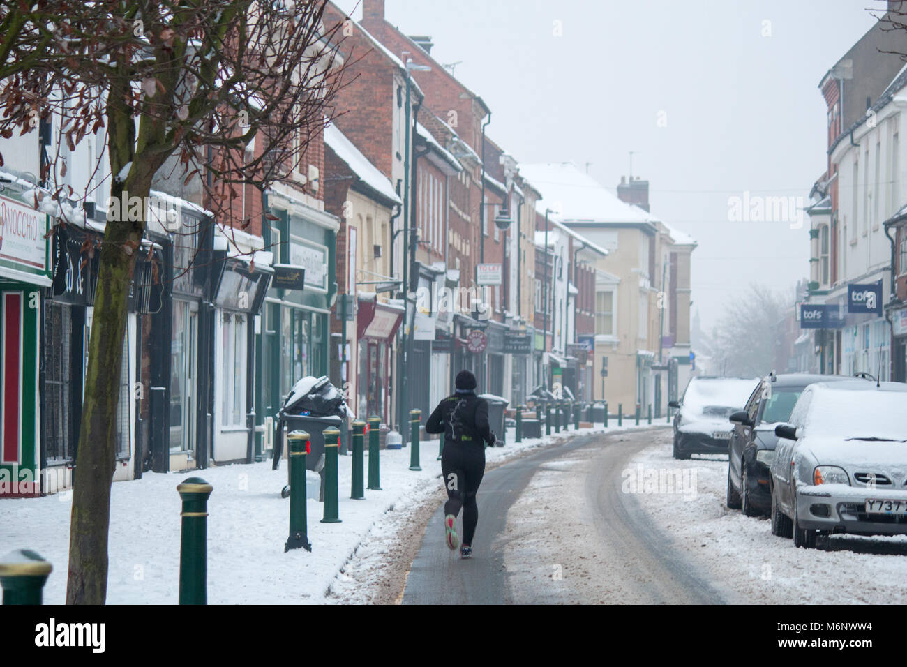 Un pareggiatore corre lungo Via in Atherstone dopo il recente la caduta di neve Foto Stock