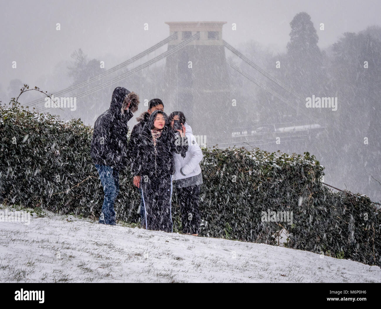Un gruppo di East Asian amici posano per una selfie con il Clifton Suspension Bridge in una tempesta di neve come sfondo - Bristol REGNO UNITO Foto Stock