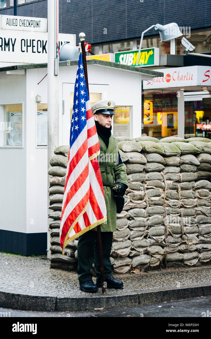 Un uomo con una bandiera americana sta di guardia al Checkpoint Charlie, Berlin, Germania Foto Stock