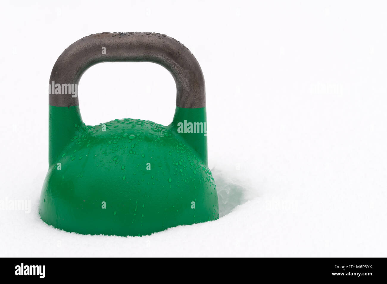 Peso verde kettlebell training coperto con le goccioline di acqua al di fuori nella neve. Copia di potenziale spazio alla destra di kettlebell. Foto Stock