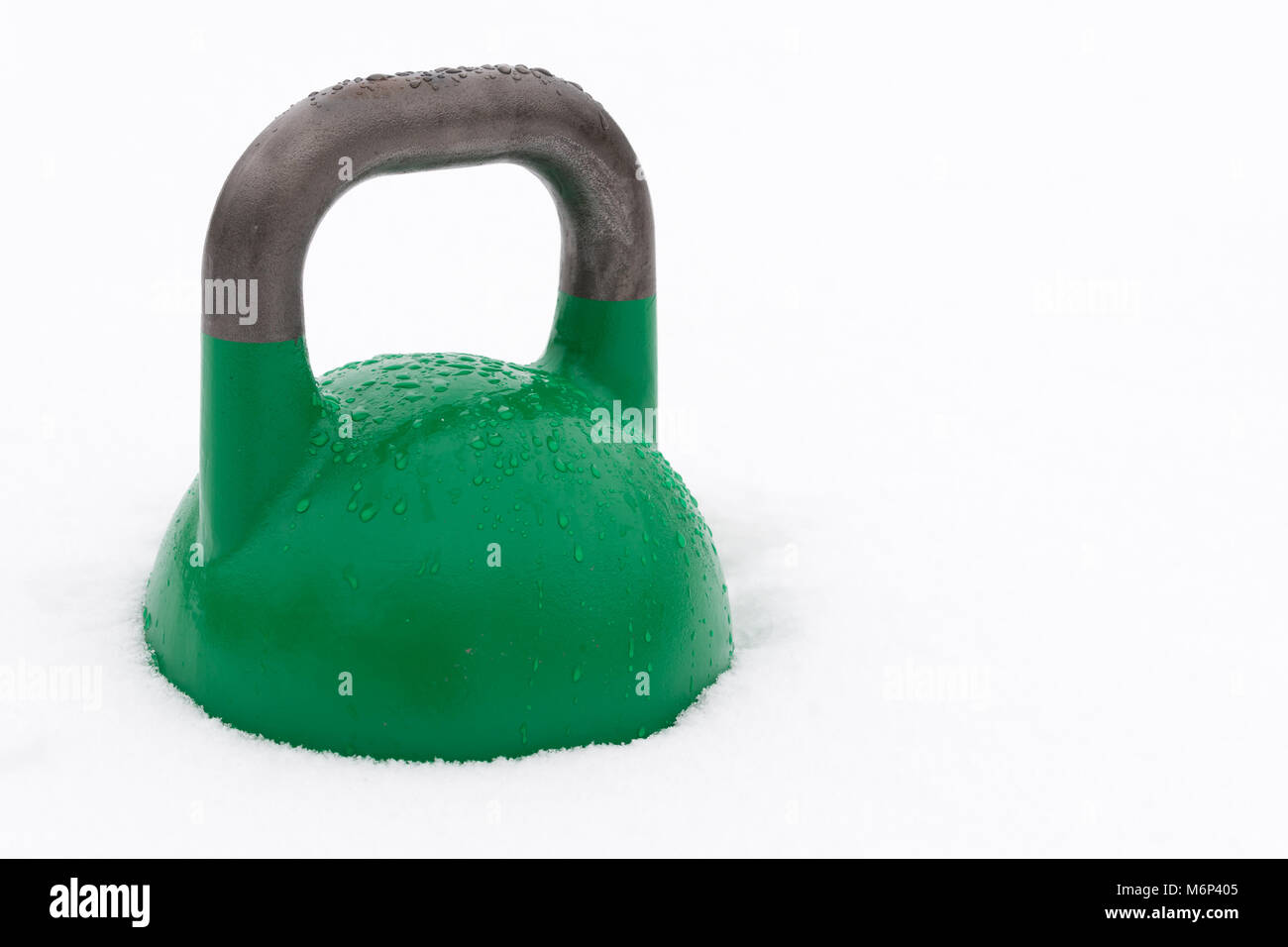 Concorrenza verde kettlebell coperto con le goccioline di acqua al di fuori nella neve. Copia di potenziale spazio alla destra di kettlebell. Foto Stock