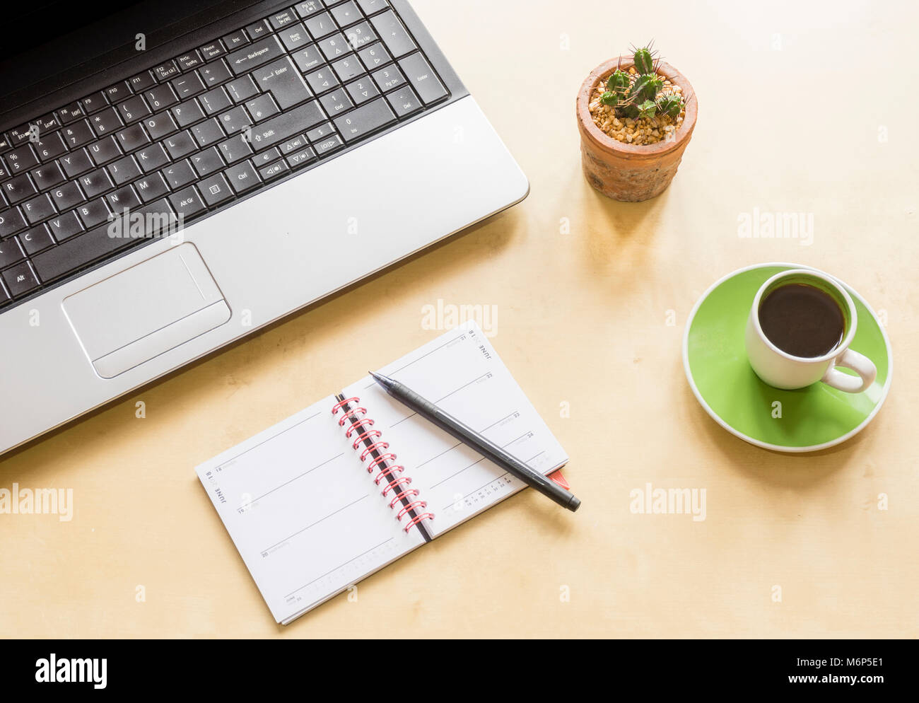 Alta angolazione di un ufficio a casa scrivania con computer portatile, cactus pianta, tazza da caffè con piattino e un calendario con penna Foto Stock