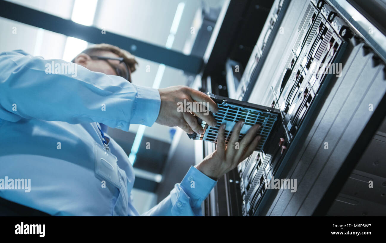 Angolo lungo girato in completo di lavoro centro dati del tecnico IT di installare il disco rigido nel rack di server. Dettagliati e precisi tecnicamente riprese. Foto Stock