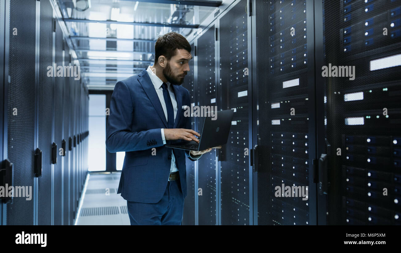 Tecnico IT nel Data Center sta prima di server Rack a lavorare sul suo computer portatile. Esegue i programmi di diagnostica o il lavoro di manutenzione. Foto Stock