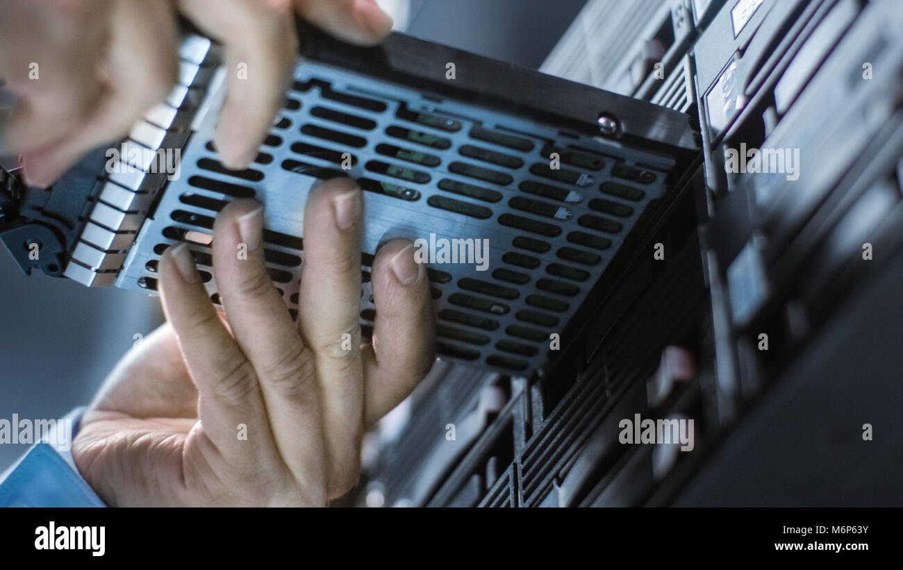 Bassa Angolazione In Completo di lavoro del centro dati Ingegnere IT installa il disco rigido in rack di server. Dettagliati e precisi tecnicamente riprese. Foto Stock