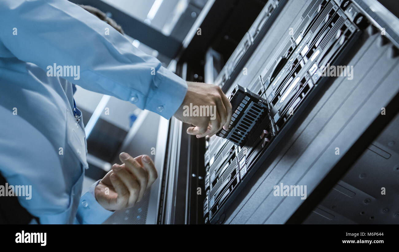 Angolo lungo girato in completo di lavoro del centro dati Ingegnere IT installa il disco rigido in rack di server. Dettagliati e precisi tecnicamente riprese. Foto Stock