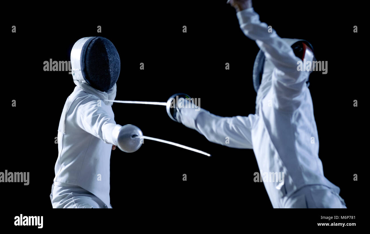Due professionale schermitori mostrano Swordsmanship magistrale nella loro lotta di lamina. Essi attaccano, difendere, Leap e spinta affondo e. Shot isolato su nero Foto Stock