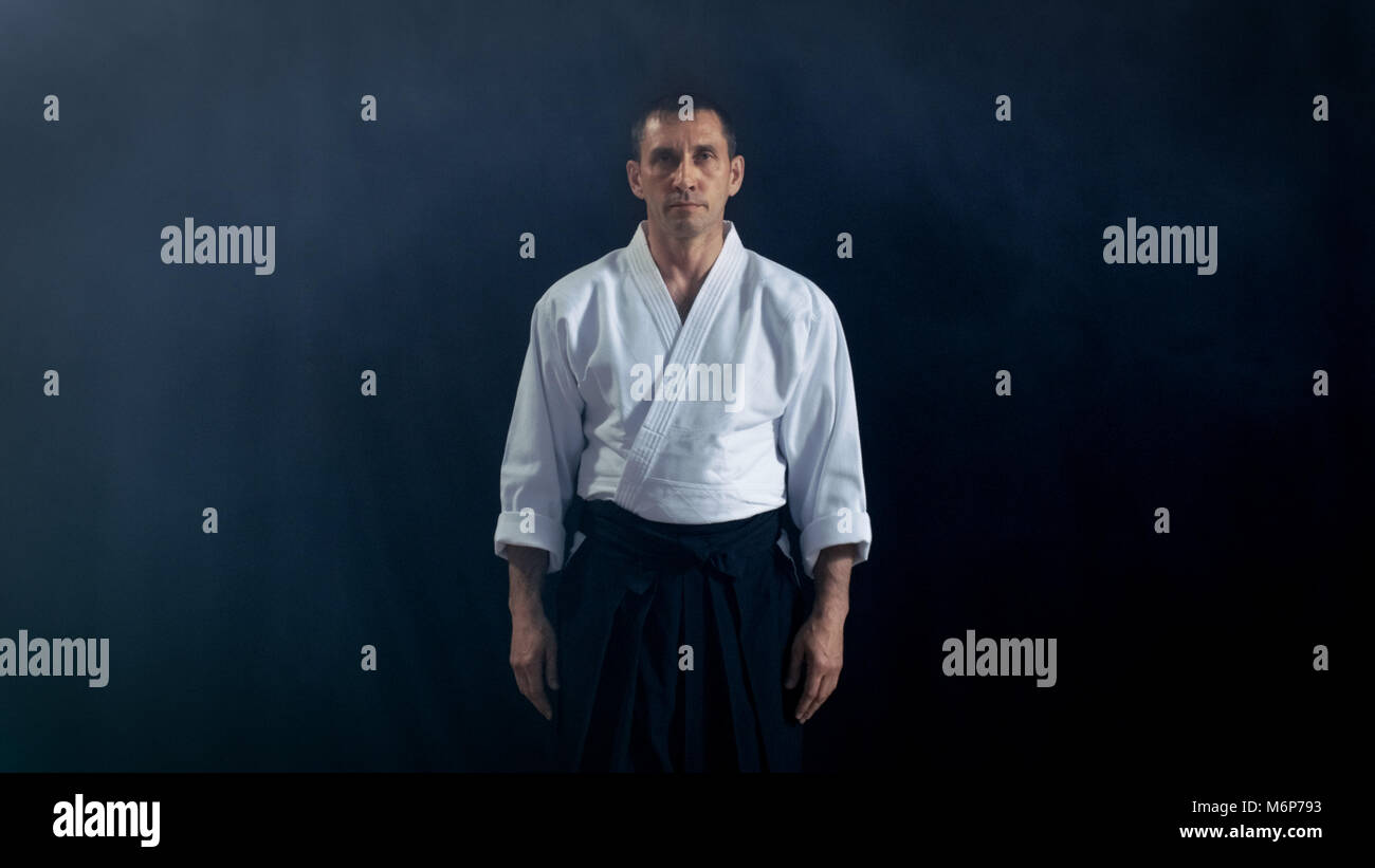 Ritratto di Aikido Master indossando il tradizionale Samurai Hakama vestiti guardando nella telecamera. Lui è sotto i riflettori il buio lo circonda. Foto Stock