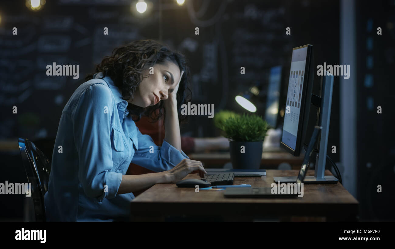Stanchi, affaticati finanziere femmina trattiene la sua testa nelle mani mentre si lavora su un Personal Computer. In Background Creative Office. Foto Stock