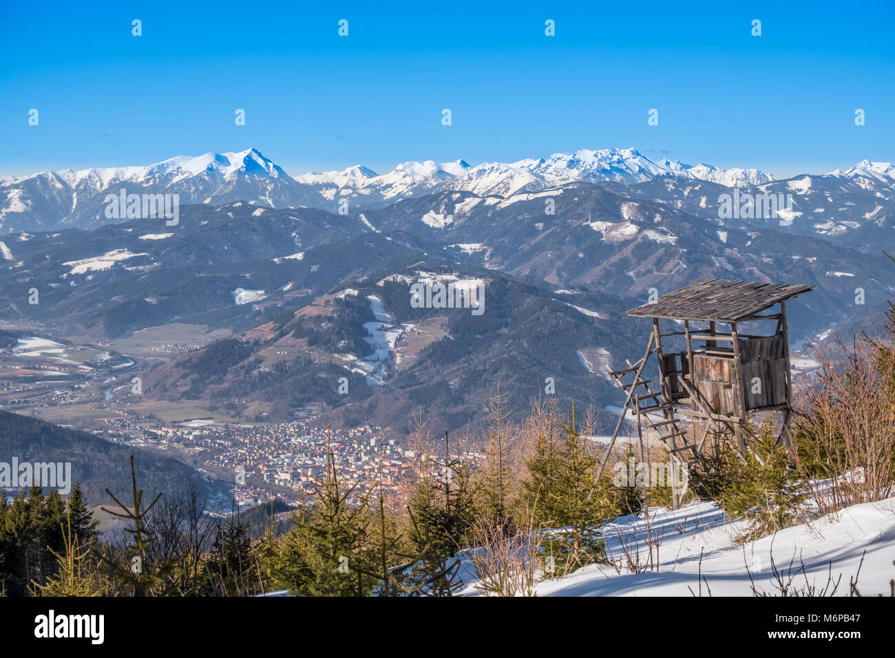 Torre di avvistamento sulla montagna innevata Rennfeld vista sulla vallata Muerztal con città di Bruck an der Mur a montagne Goesseck, Stadelstein e Eisenerzer Reichens Foto Stock