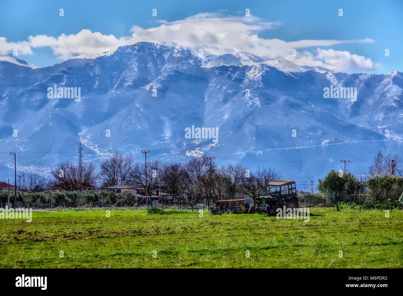 Vecchio trattore sul campo con lo sfondo di una montagna innevata Foto Stock