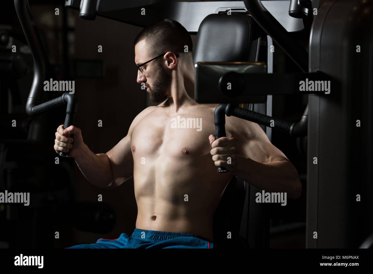 Bello il Fitness muscolare uomo che indossa gli occhiali facendo Peso pesante esercizio per il torace sulla macchina con cavo in palestra Foto Stock