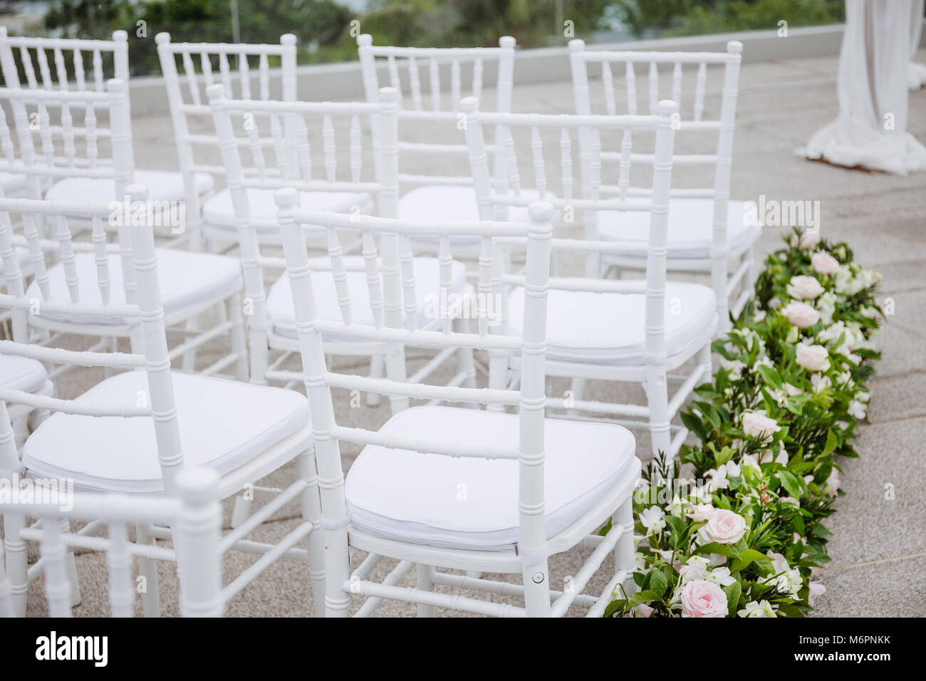 Legno bianco sedie di Chiavari line up decorato con fiori in corridoio Foto Stock