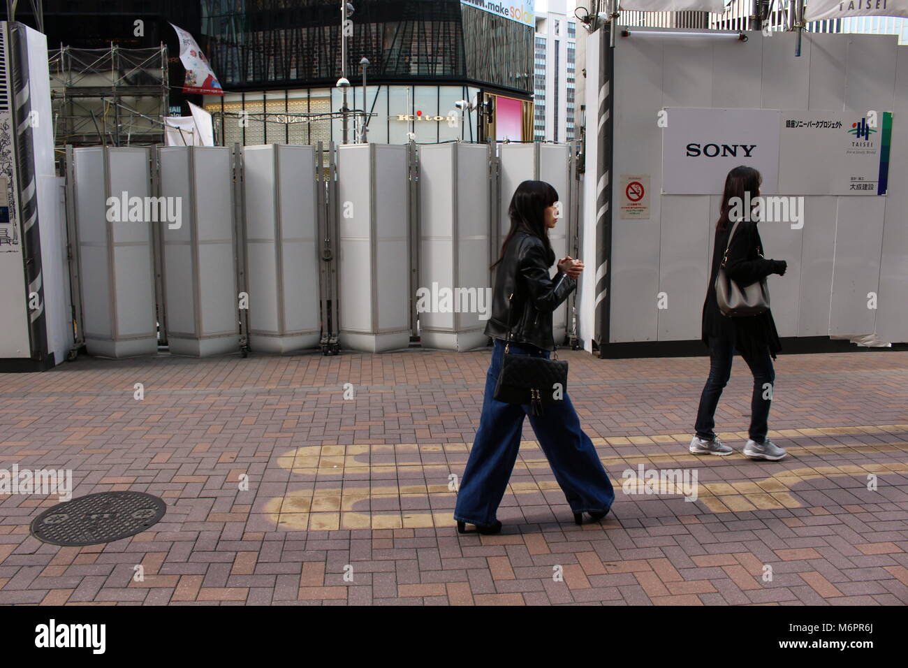 La gente a piedi oltre la recinzione temporanea attorno al sito dell'oggi demolita Sony Building di Ginza. Il sito sarà trasformato in un parco. (Marzo 2018) Foto Stock