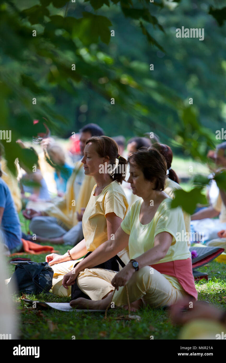 Le donne sedute sull'erba sotto agli alberi in posizione di parcheggio la pratica di meditazione con gambe incrociate. Foto Stock