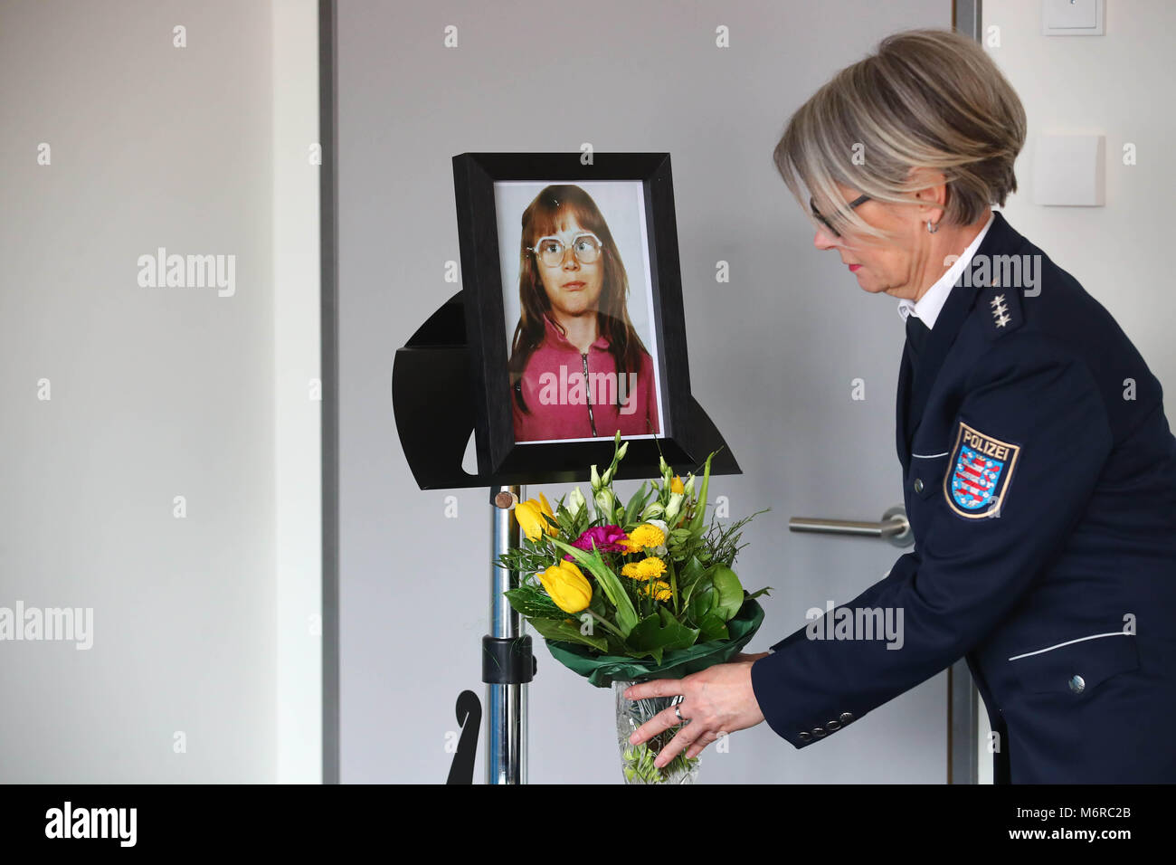 06 marzo 2018, Germania, Jena: un funzionario di Jena e di polizia presentando un mazzo di fiori sotto la foto del assassinato Stephanie Drews davanti a una conferenza stampa dalla polizia di Jena. La ragione per la conferenza stampa è la risoluzione del 1991 caso di Stephanie ha richiamato l'assassinio. Un uomo sospettato del crimine è stato arrestato come parte dell'inchiesta. Il caso è il più antico dei tre casi di omicidio del bambino in Jena e Weimar sotto inchiesta da parte della commissione speciale 'fredda casi" dal novembre 2016. Foto: Bodo Schackow/dpa-Zentralbild/dpa Foto Stock