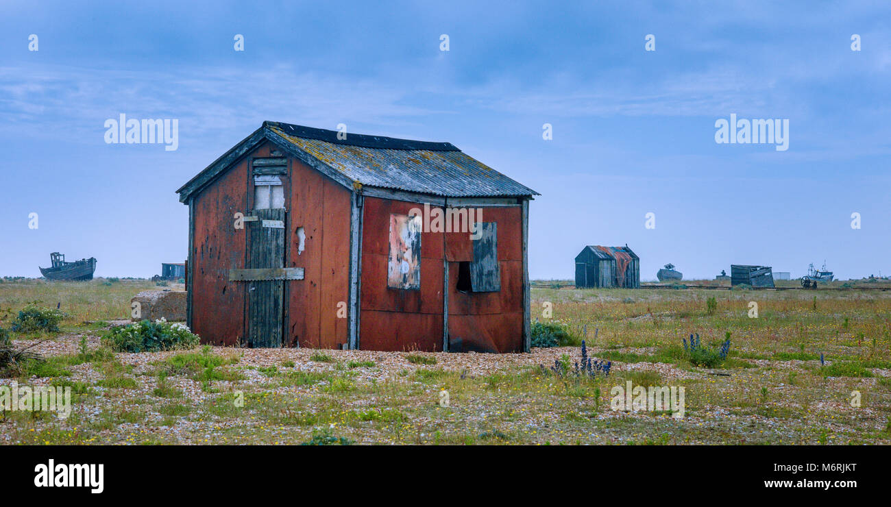 Fishermens capanne e il le carcasse delle vecchie barche lettiera la spiaggia di Dungeness. Foto Stock