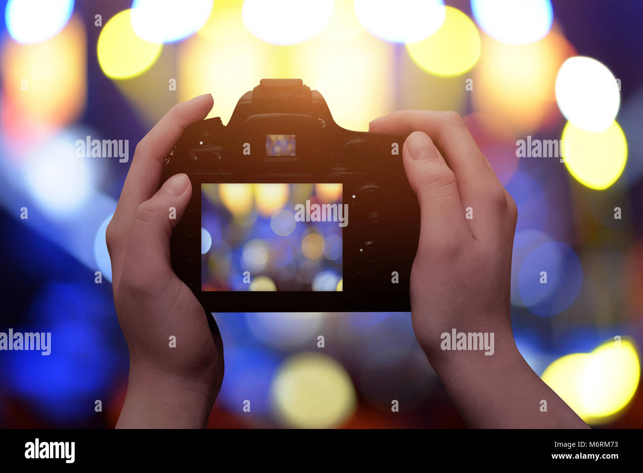 Profesional fotocamera digitale nelle mani. Il blu e il giallo bokeh in background. Foto Stock