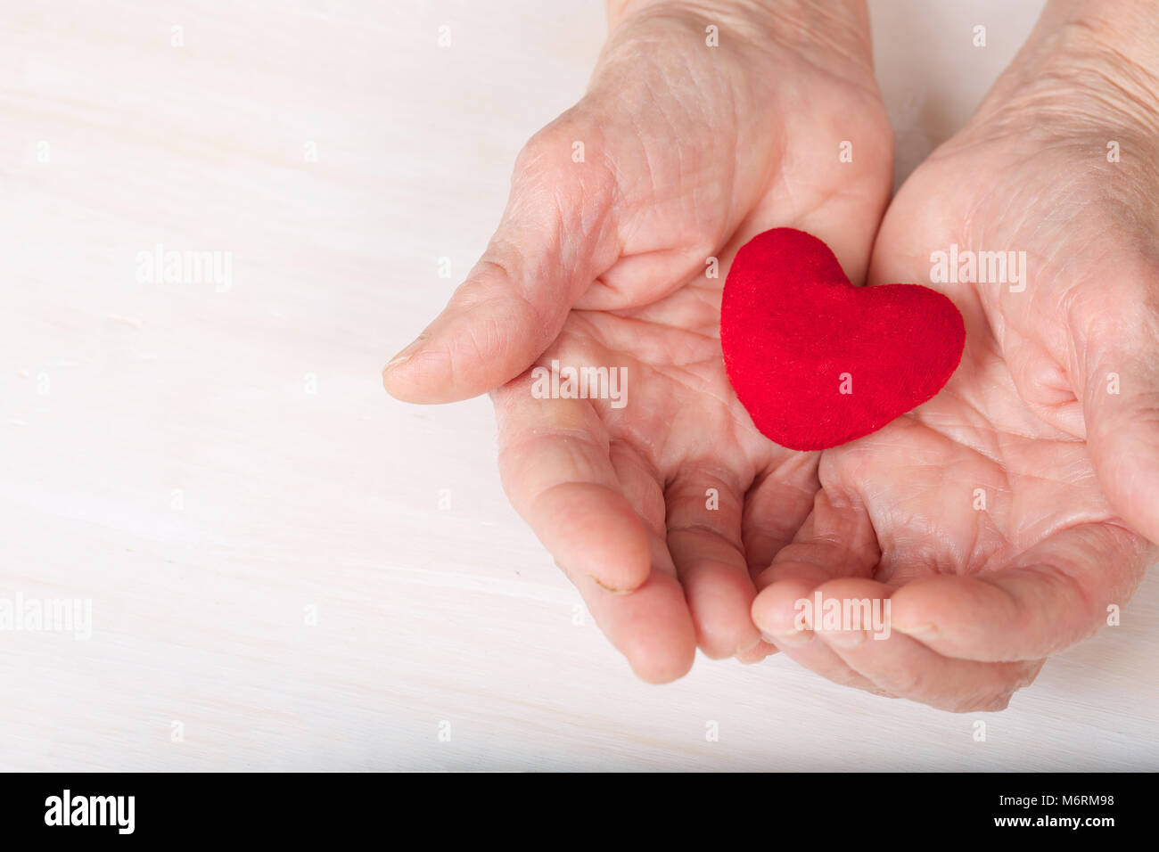 Vecchia donna mantiene un morbido cuore rosso nel suo palms Foto Stock