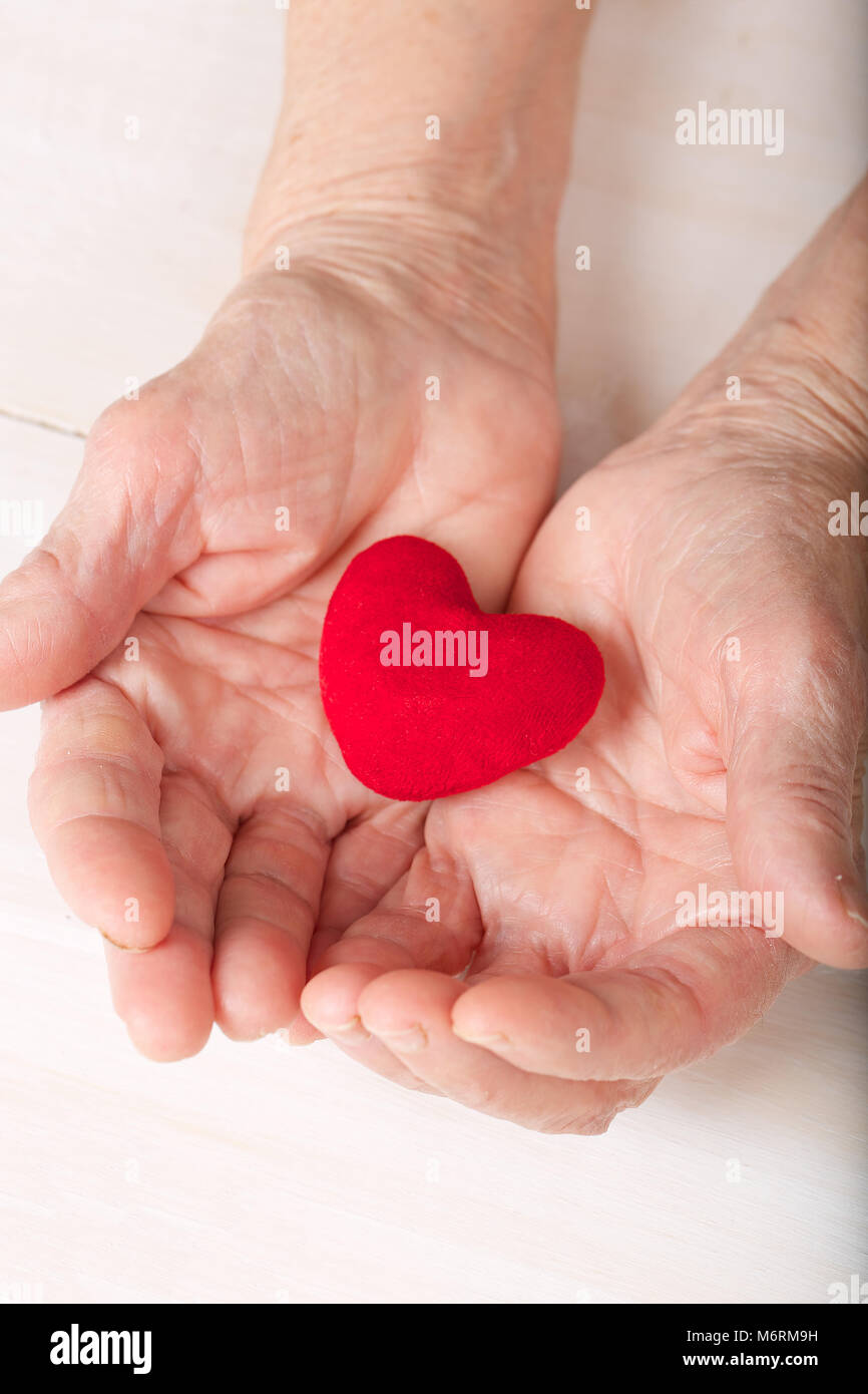 Vecchia donna mantiene un morbido cuore rosso nel suo palms Foto Stock