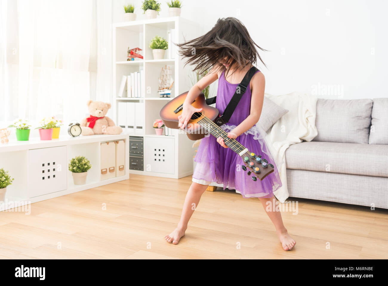 La femmina kid giocando in salotto immaginare se stessa un super rock star. Scuotendo la testa in modo duro e godersi la musica di sottofondo. Foto Stock