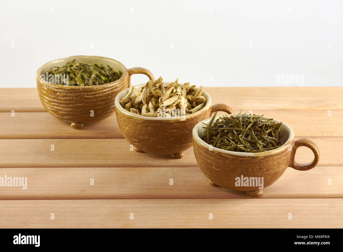 Tre tazze con verde bianco e le foglie di tè su sfondo bianco Foto Stock