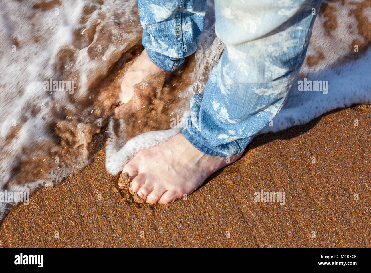 Una donna in jeans pagaie sulla spiaggia sabbiosa a Seaton Sluice, senza scarpe, Northumberland, Regno Unito Foto Stock