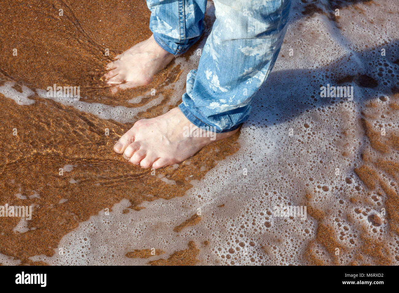 Una donna in jeans pagaie sulla spiaggia sabbiosa a Seaton Sluice, senza scarpe, Northumberland, Regno Unito Foto Stock