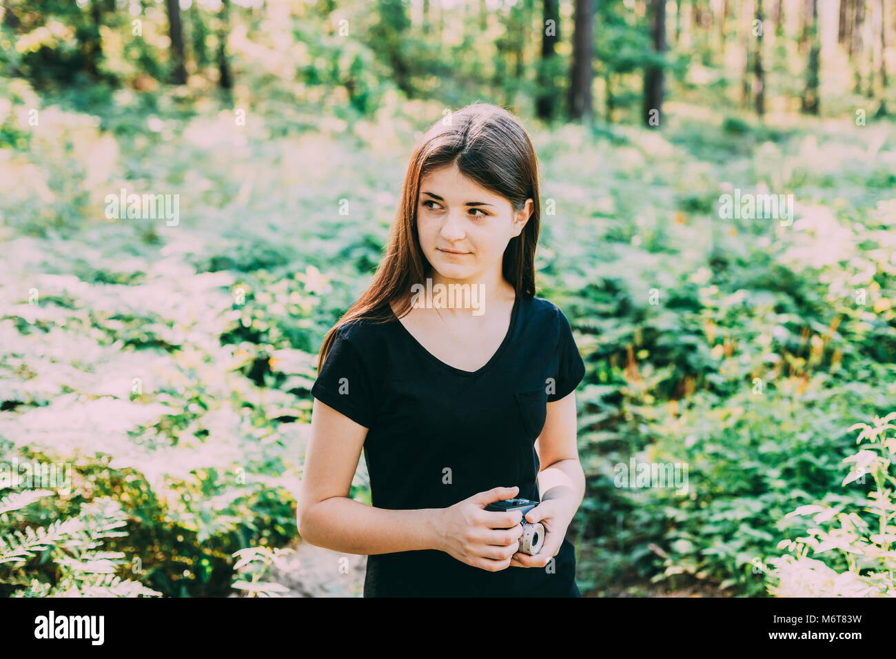 Felice giovani i capelli rossi Caucasian ragazza adolescente fotografo fotografare il vecchio Retro Vintage fotocamera a pellicola in estate foresta verde. Ragazza vestita di un Foto Stock