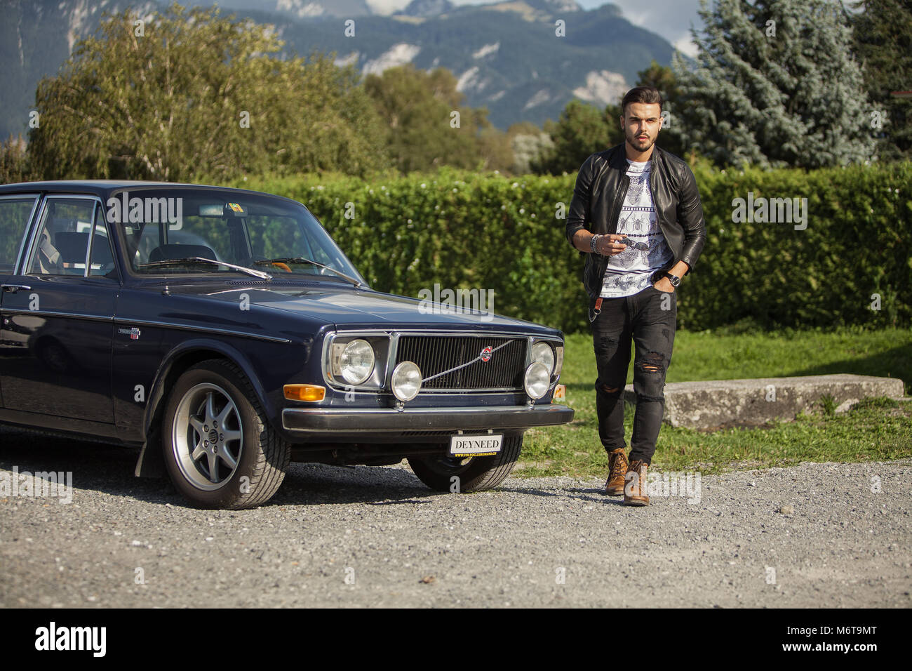 Uomo con stile (giacca di pelle, cuoio boot) raffreddamento con una vecchia auto Foto Stock