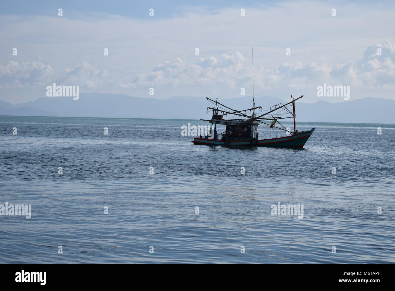 Un isolato di piccole barche di pescatori nel Golfo di Thailandia non lontano da Koh Tao su un mare limpido con le montagne e le nuvole in background. Foto Stock