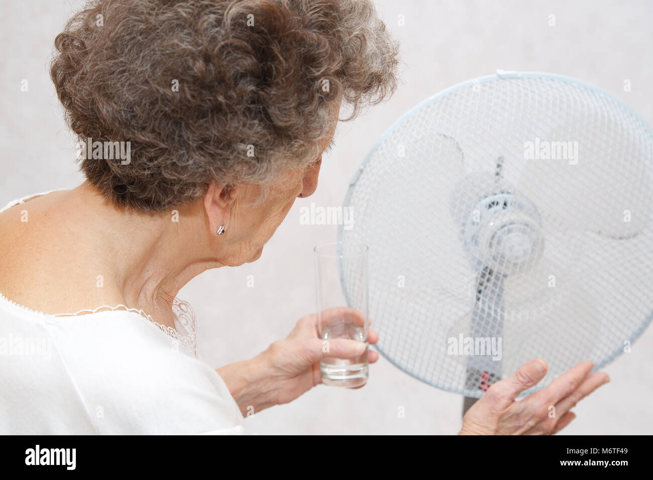 Senior donna tra 70 e 80 anni resta vicino al ventilatore. Soffre di calore Foto Stock