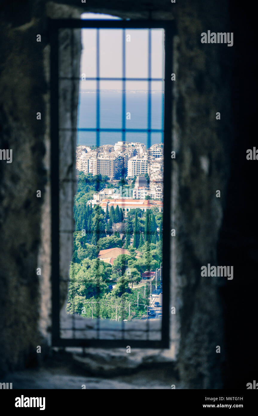La vista di una cella di prigione sbarrate finestra in una vecchia prigione  rovina alla città moderna di paesaggio. Dietro le sbarre la visualizzazione  della finestra verso il mondo esterno Foto stock -