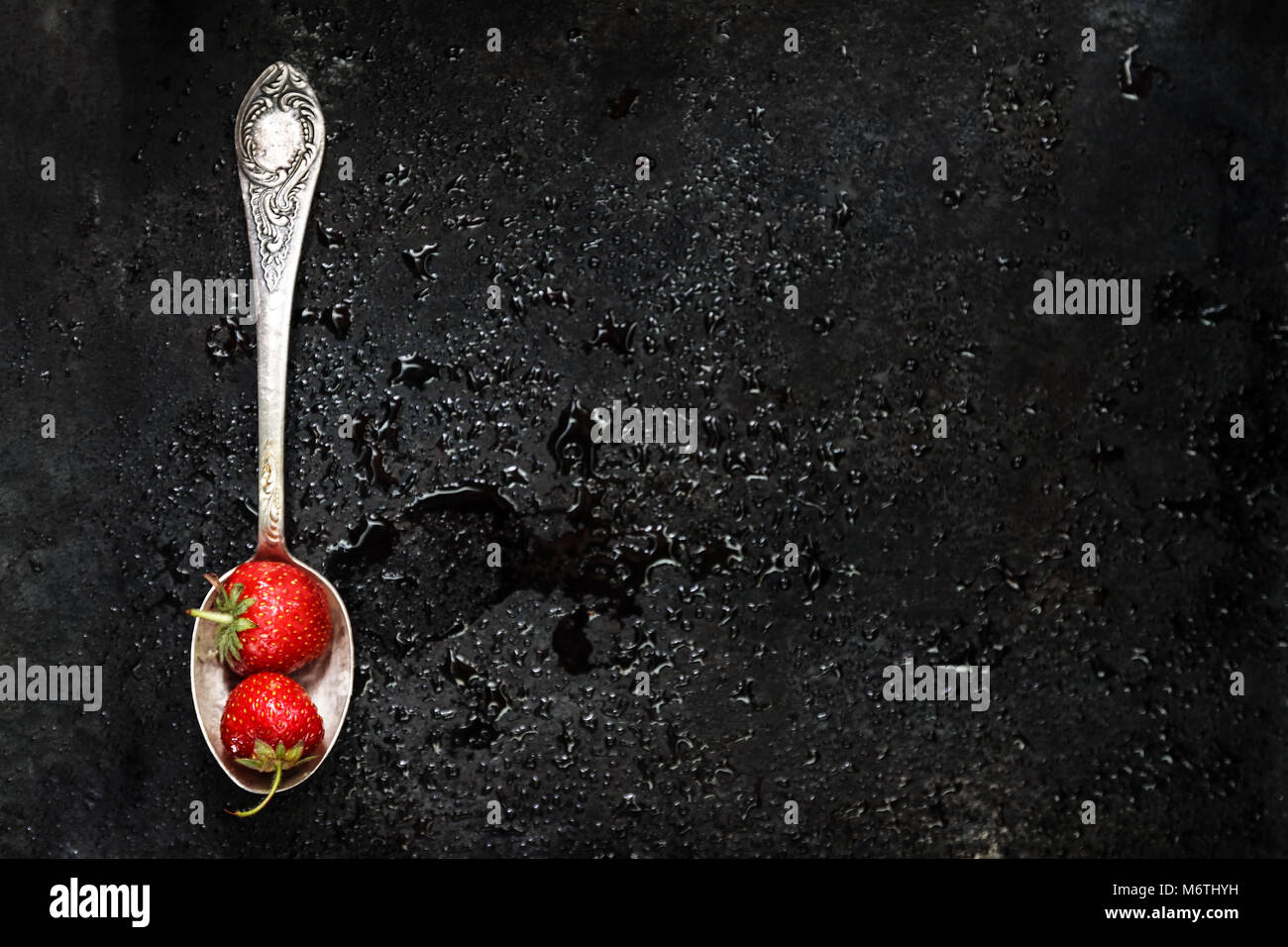 In un cucchiaio una fragola umido su sfondo scuro con spruzzi di acqua, vista dall'alto. Foto Stock