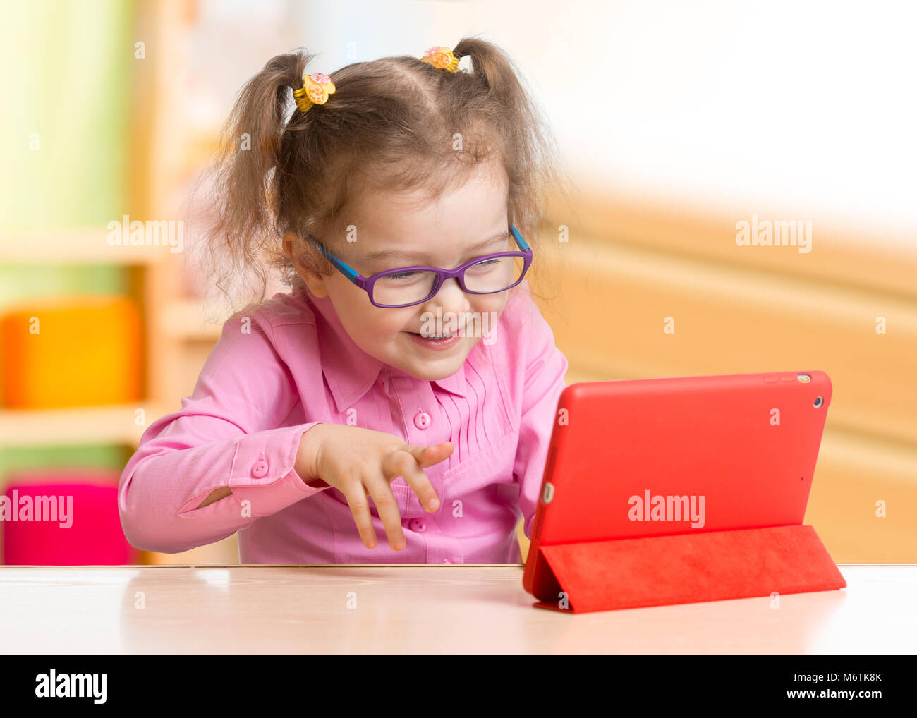Smart kid in occhiali utilizzando tablet PC o un e-libro seduti a tavola nella sua camera da letto Foto Stock