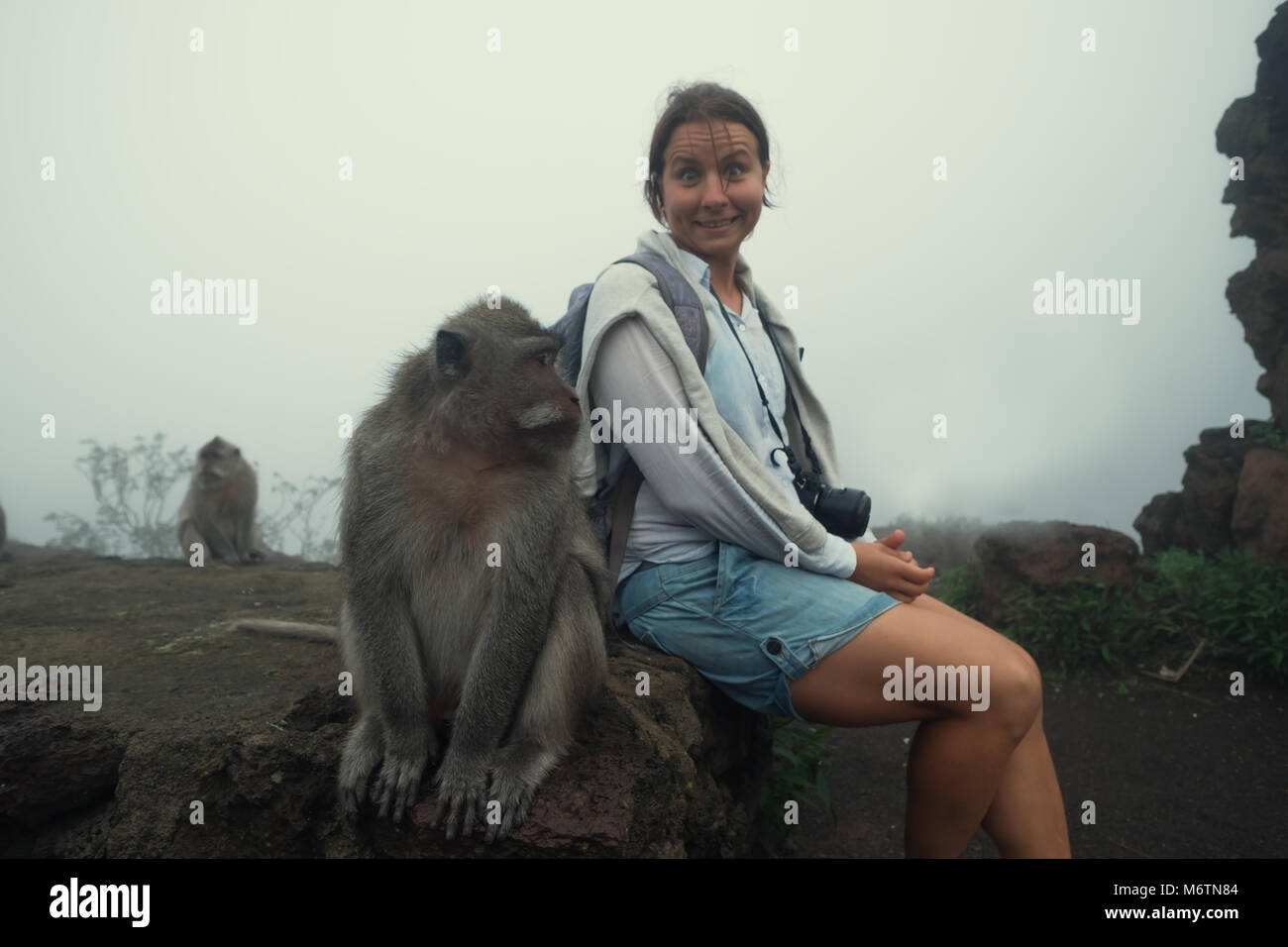 La donna caucasica in un pantaloncino seduta vicino scimmia. Lei è un po' di paura di essa. Turistico con la fauna locale in Indonesia Foto Stock