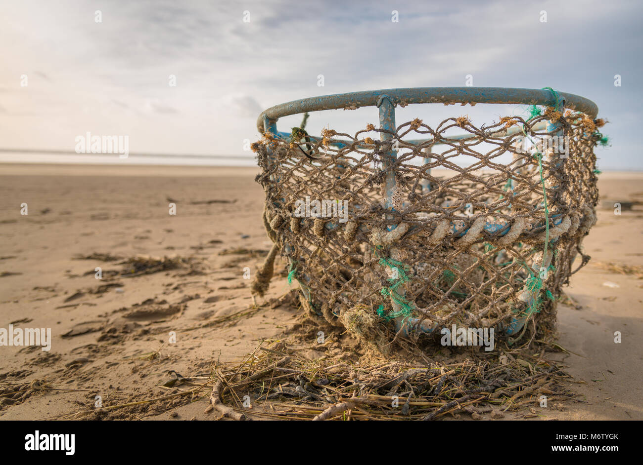 Una alta marea si lascia alle spalle i detriti compresi danneggiato lobster trappola sulla Cefn Sidan. Carmarthenshire, West Wales. Regno Unito. Foto Stock