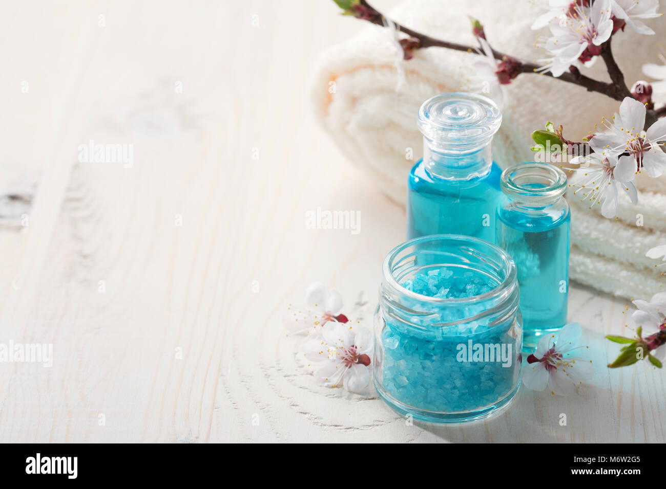 Bagno minerale sali, gel doccia, asciugamani e fiori sul tavolo di legno. DOF poco profondo. Focus sul sale. Foto Stock