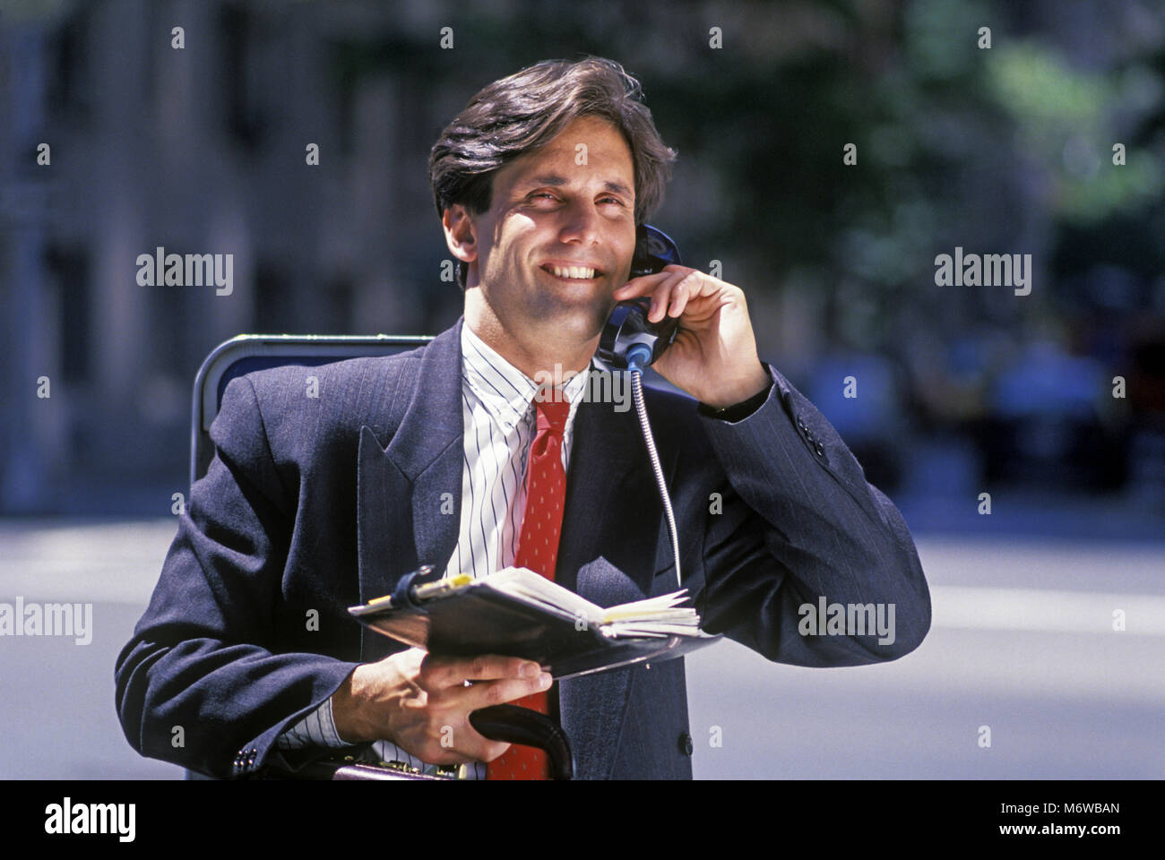 1994 STORICO SORRIDENTE UOMO D' AFFARI CAUCASICO AL TELEFONO PUBBLICO A PAGAMENTO (©ATT 1994) CHE DETIENE FILOFAX CARTA ORGANIZZATORE (©LETTS FILOFAX GRUPPO 1994 ) Foto Stock