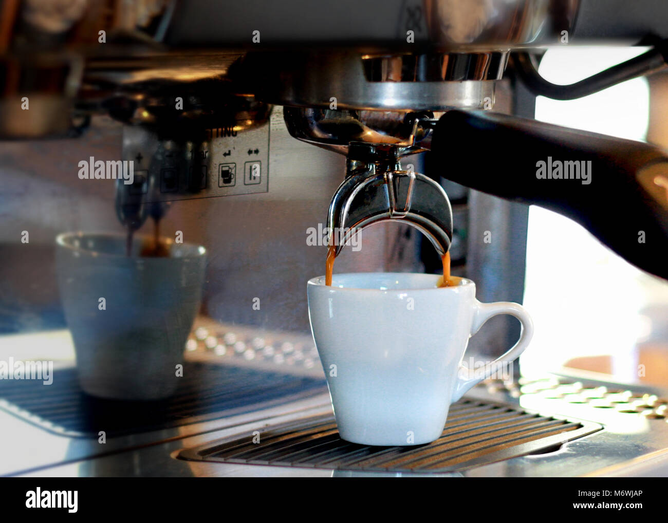 Una macchina espresso gocciola caffè ricco in una tazza bianca. Foto Stock