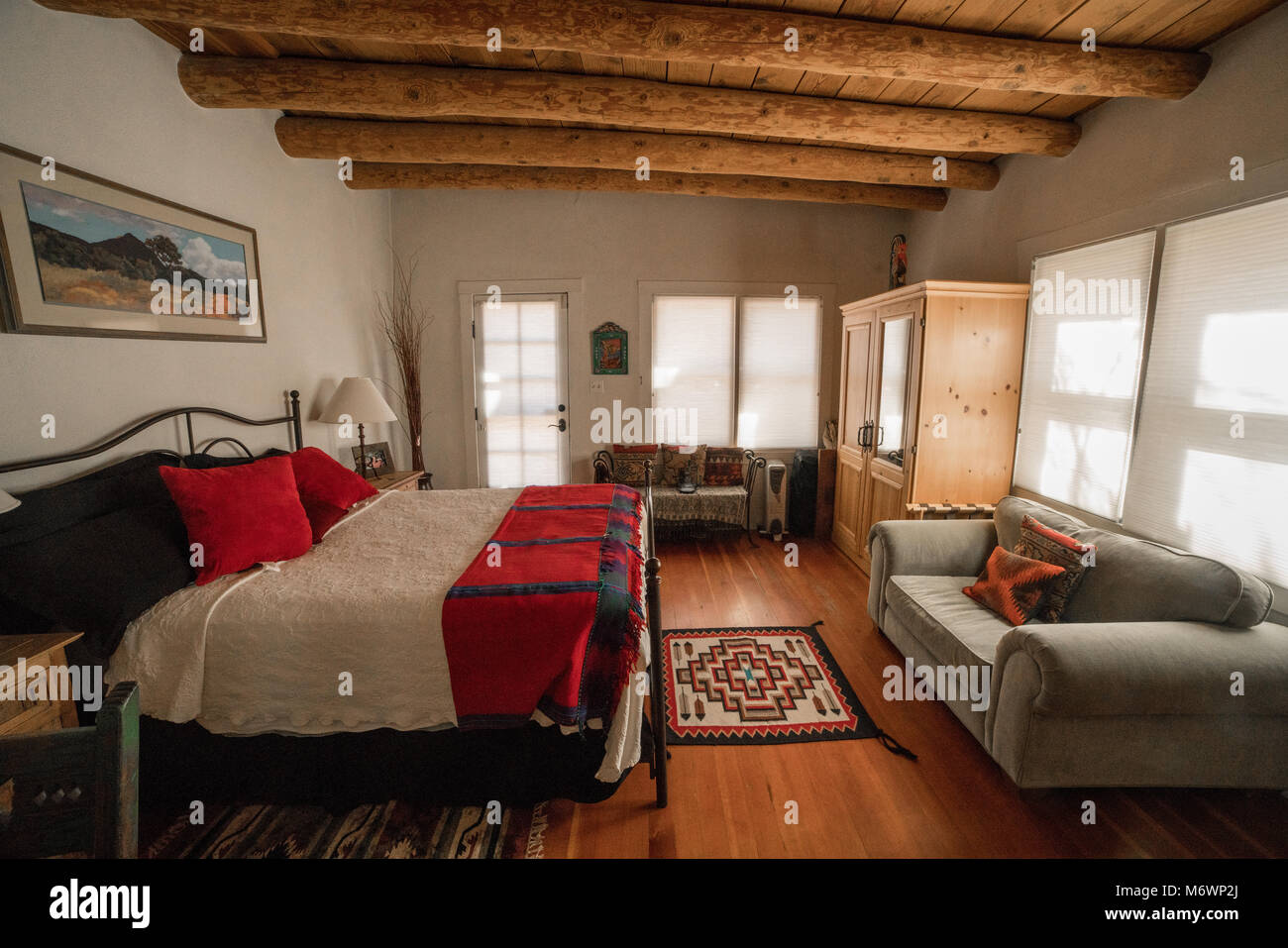Una pittoresca Santa Fe, New Mexico camera da letto in un adobe architettura stile casa con pavimenti in legno, log dei soffitti e pareti bianche. Foto Stock