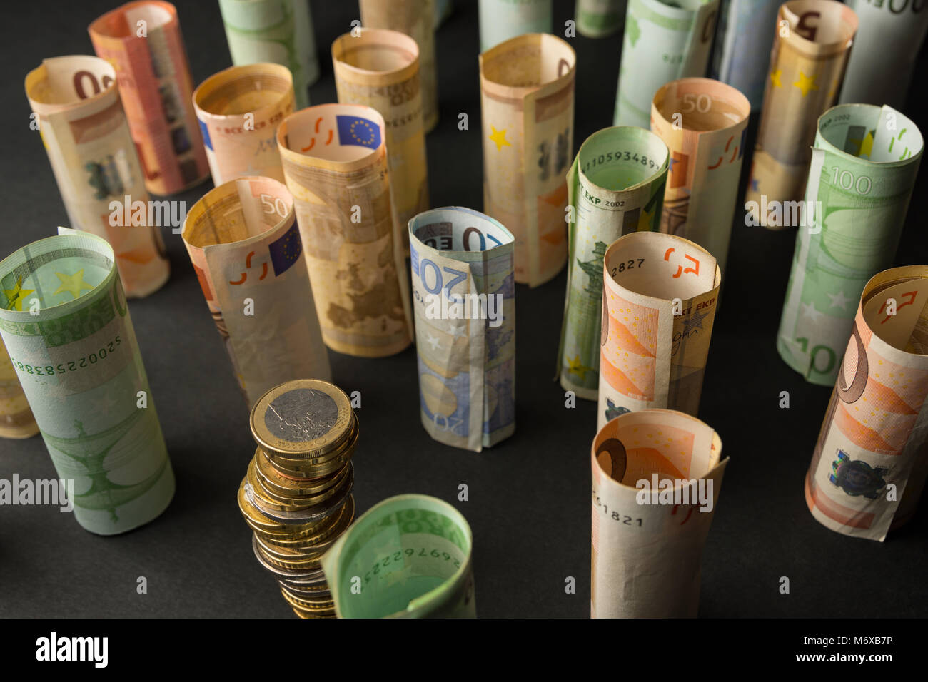 Pila di monete metalliche in euro e rotoli di banconote in background Foto Stock
