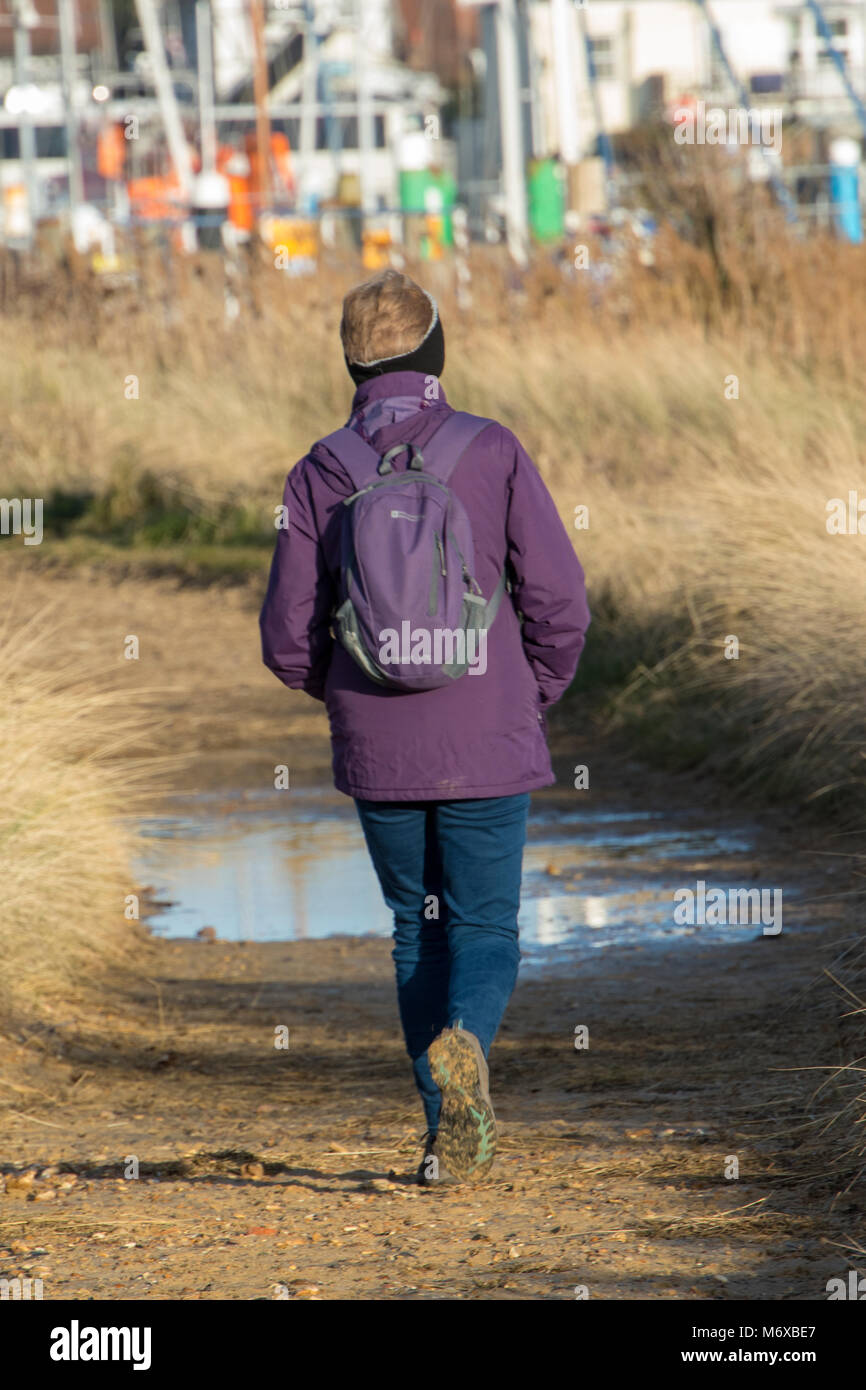 Un vecchio o donna di mezza età o signora a piedi lungo una strada di campagna avvicinando una pozza sul sentiero o via. esercizio in età avanzata e delle escursioni. Foto Stock